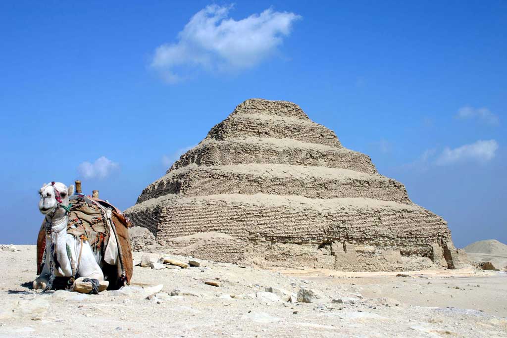 The picture is that of Djoser's stepped pyramid. The pyramid includes five mastabas stacked on top of one another like a pyramidal layer cake. A camel sits in front of the pyramid.