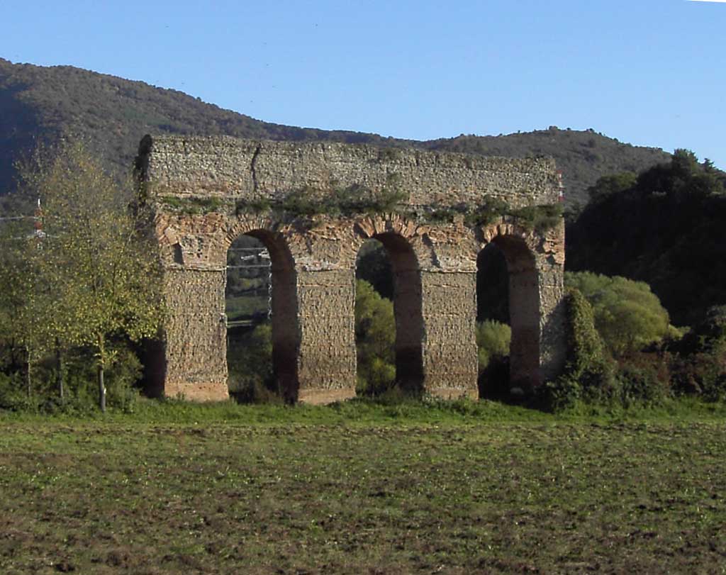 Picture of the Aqua Marcia standing in an open field. Only four arches of the concrete aqueduct remain.