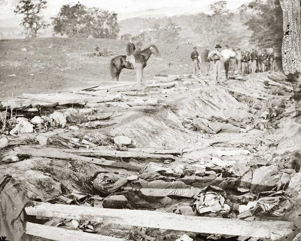 Confederate dead at Bloody Lane, looking northeast from the south bank; the Union soldiers looking on were likely members of the 130th Pennsylvania, who were assigned burial detail