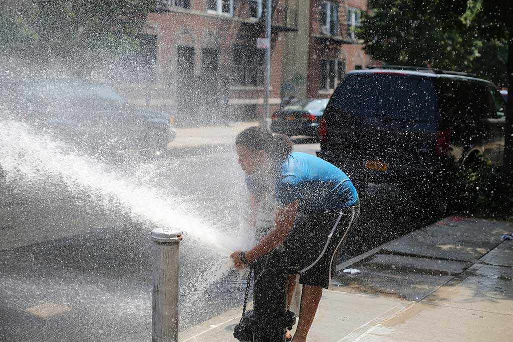 Young man spraying water out of a fire hydrant on a city street.