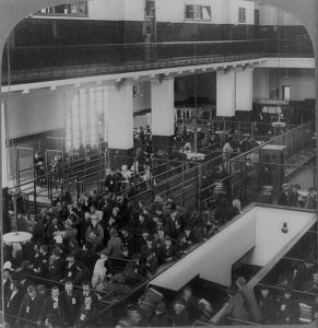 Black and white vintage photo of a view of the Ellis Island immigrant processing center, showing a room full of people being herded through a maze of waiting lines and gates