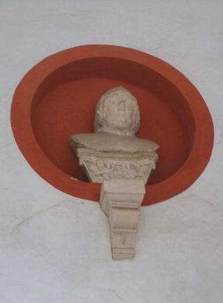 Una cabeza de piedra blanca o mármol esculpida sobre un capitel para su montaje en una pared o nicho. Es el busto que originalmente presidía la “Calle del Candilejo” por orden de Pedro I.