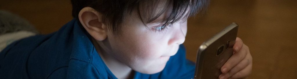El resplandor de un teléfono inteligente brilla en la cara de un niño pequeño