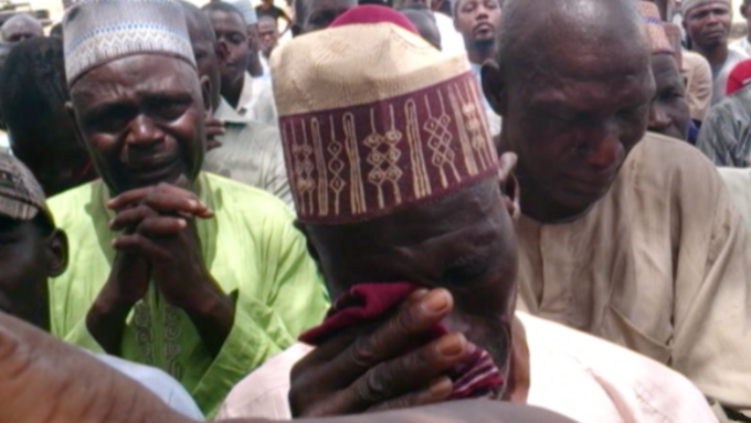The photograph shows three men in a crowd crying and praying.