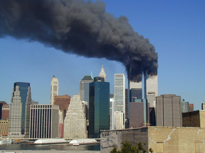 The former World Trade Center in Lower Manhattan during September 11 attacks in 2001. Both are on fire and smoking heavily.