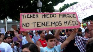 Photo of a young man holding a sign that reads "Tienen miedo porque no tenemos miedo"