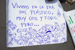 Photo of a handwritten sign reading "Vivimos en la era del plástico, muy útil y todo, pero..." with pictures of fish with x's for eyes, surrounded by plastic bottles