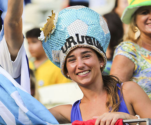 A women dressed in a blue and white soccer-ball hat that reads Uruguay.