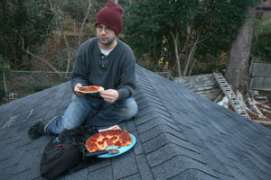A man eating pepperoni pizza on the roof of a garage in Durham, North Carolina.