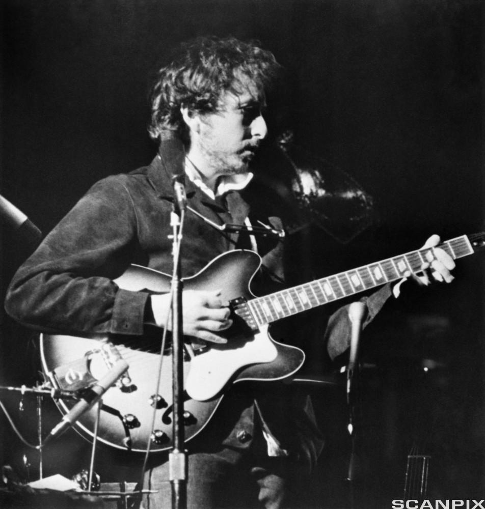 Black and white photo of Bob Dylan playing guitar on a stage
