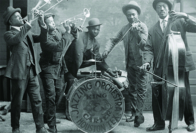 Una fotografía muestra a un grupo de músicos de jazz negro tocando sus instrumentos. Una batería dice “Jazzing Orchestra/King and Carter/Houston Tex”.