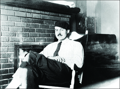 Una fotografía muestra a Ernest Hemingway reclinado en una silla frente a una chimenea.