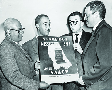 Una fotografía muestra a Henry L. Moon, Roy Wilkins, Herbert Hill y Thurgood Marshall sosteniendo un cartel que dice “¡Destapa el missipiismo! Únete a NAACP”. En medio del cartel, un gráfico muestra el estado de Mississippi con una lápida en el centro. La lápida muestra los nombres de cuatro afroamericanos asesinados en Mississippi en 1955.