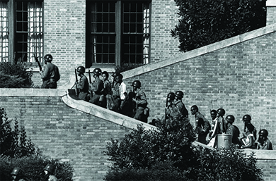 Una fotografía muestra a soldados uniformados sujetando fusiles mientras escoltan a los Little Rock Nine subiendo los escalones de la Preparatoria Central.
