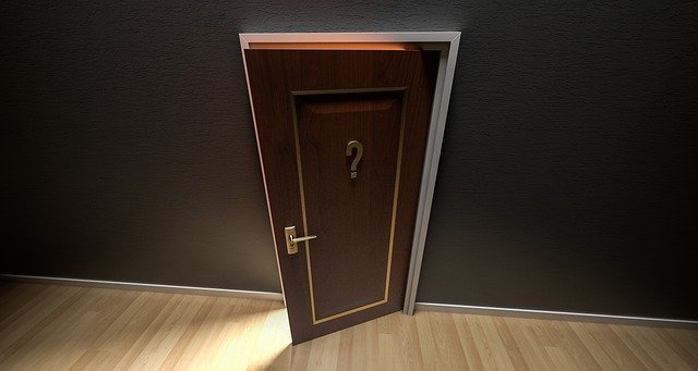 A door slightly open, letting in light. The door has a question mark on it.