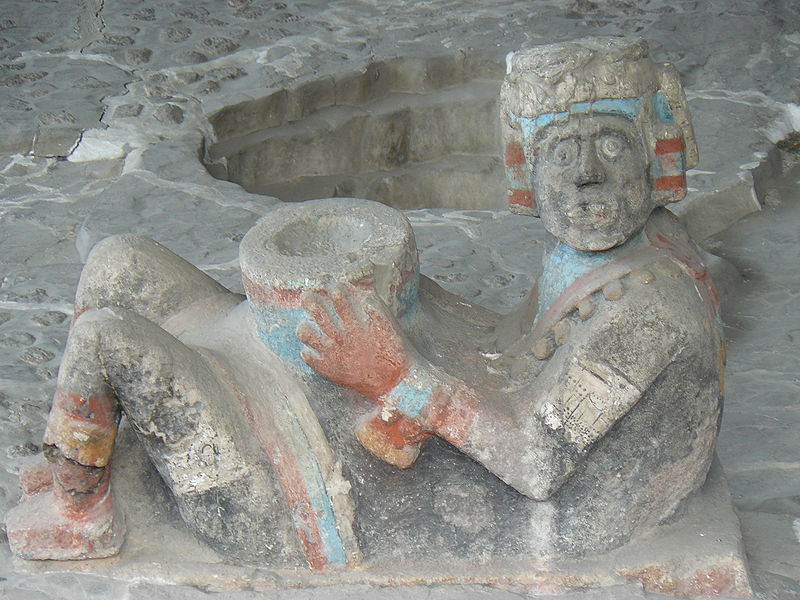 A stone carving with painted glaze of a man sitting on the ground holding a bowl