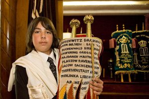 Jewish boy holding a scroll with the names of Holocaust death camps and slave labor camps at his Bar Mitzvah.