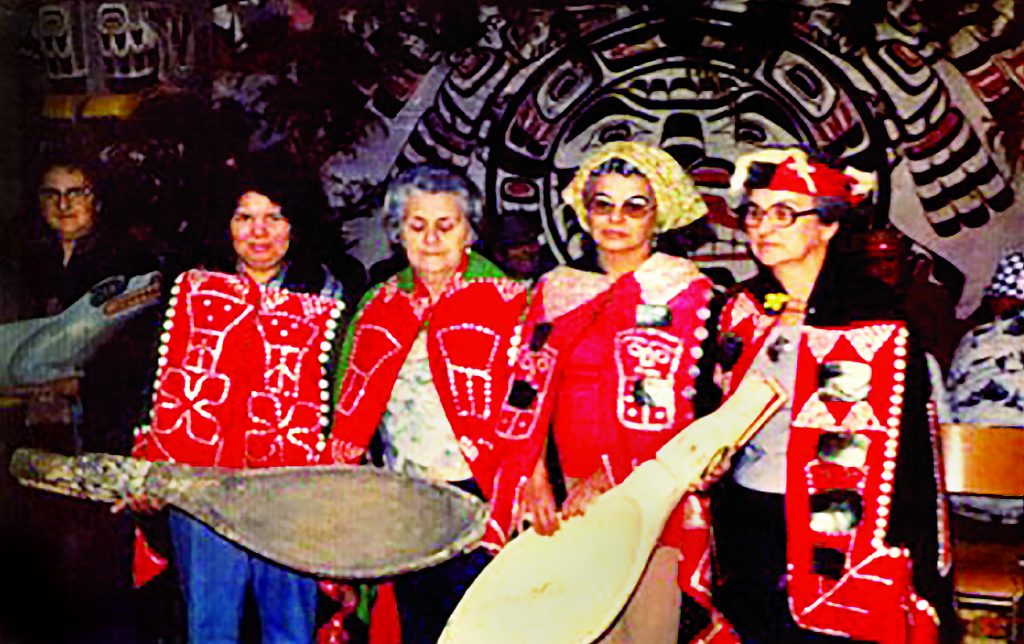 Arthur Dick’s sister Daisy Joseph, daughter Gwi'molas Vera Newman and aunties, Ethel Alfred, Stella Sumners, and cousin Christine Taylor holding grease spoons and wolf feast dish at a T'łi'nagila (grease feast) he hosted