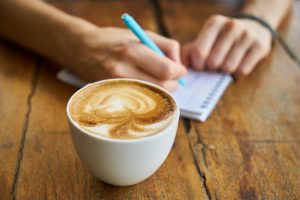 man's hands writing on notepad wood plank table espresso coffee