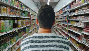 back of man as he walks down supermarket aisle