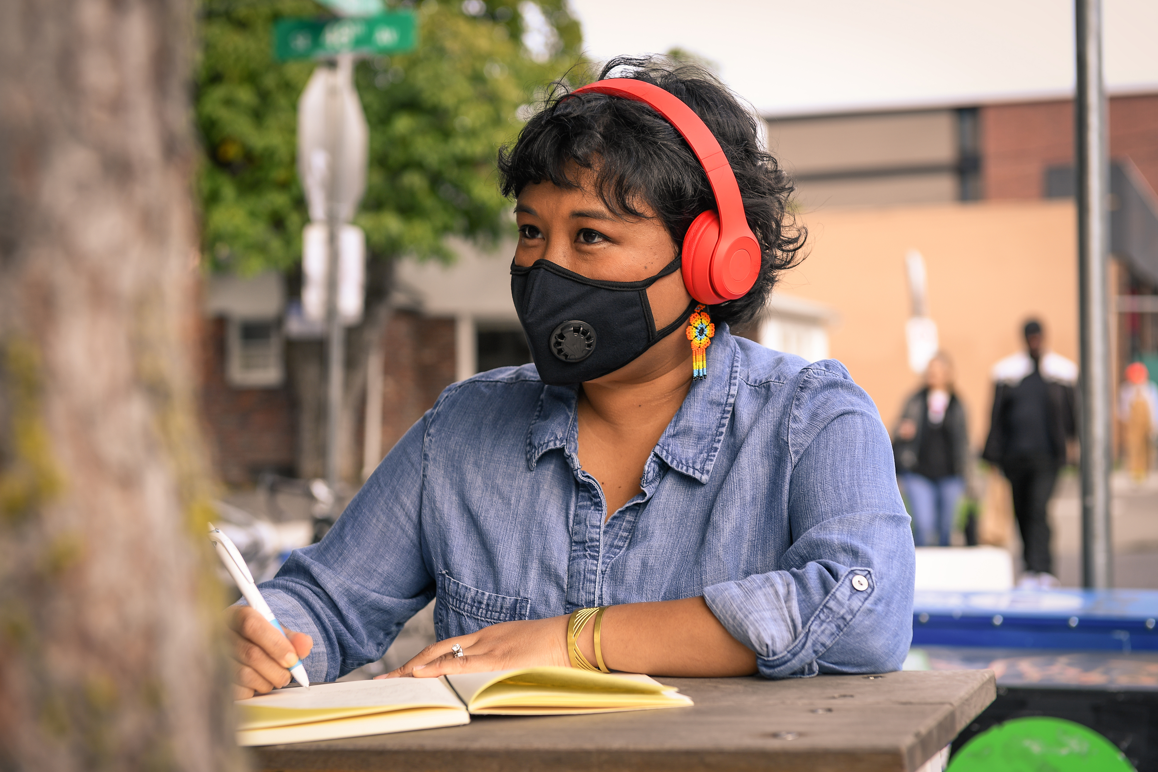 A Filipinx woman with a filtering face mask, sitting at a table with notebook and pen.