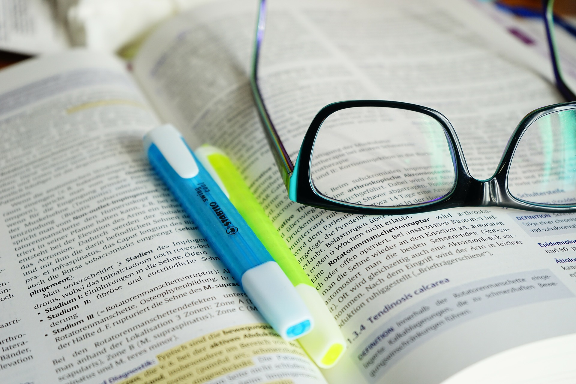 Ouvrage académique ouvert sur une page surlignée. Au sommet du livre se trouvent deux surligneurs et une paire de lunettes.
