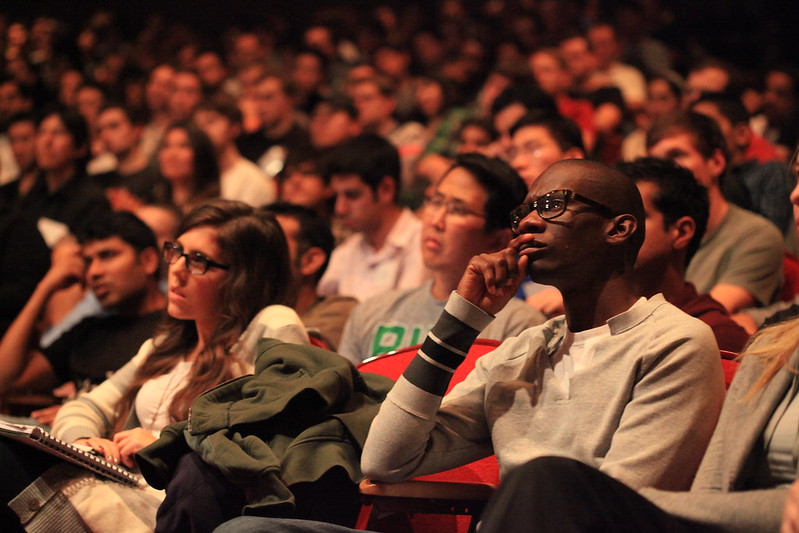 Un auditorio lleno de jóvenes racialmente diversos luciendo pensativos.