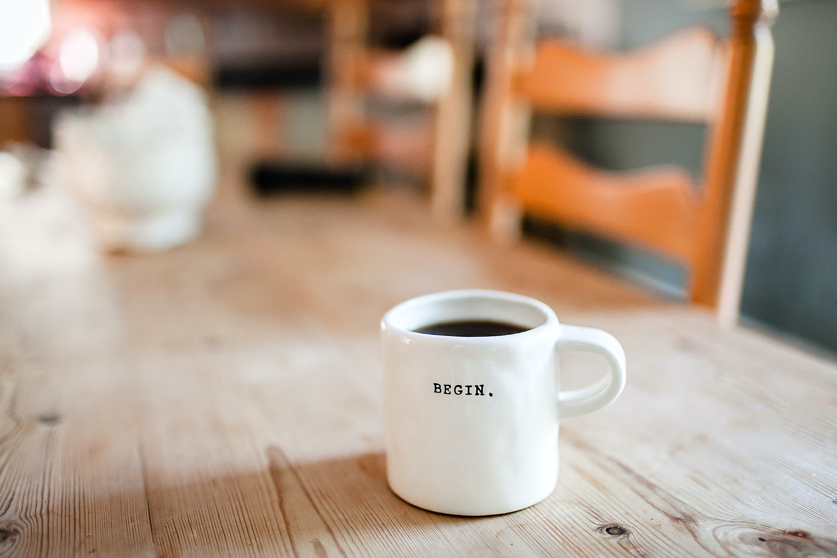 Une tasse sur laquelle est inscrit le mot « Begin », remplie de café sur une table.