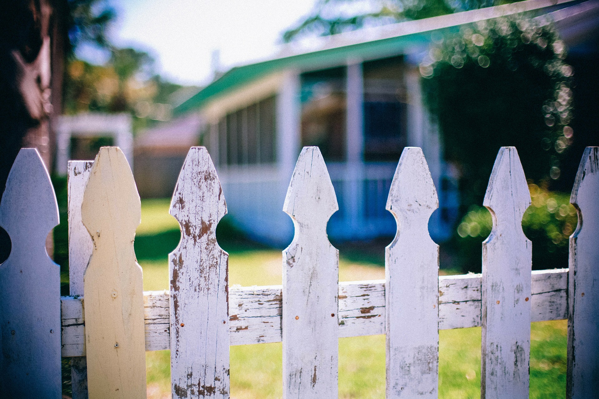 An old white picket fence around a back yard.