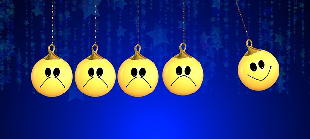 A series of emoji faces on round ornaments hung from strings.  The first several are hanging still and frowning and the final one is in motion, smiling.