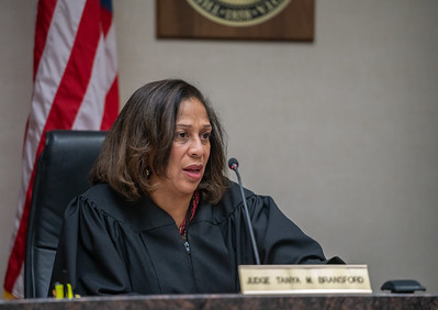 Middle-aged woman of color in judge's robes speaks into a microphone with a serious expression, a flag behind her.
