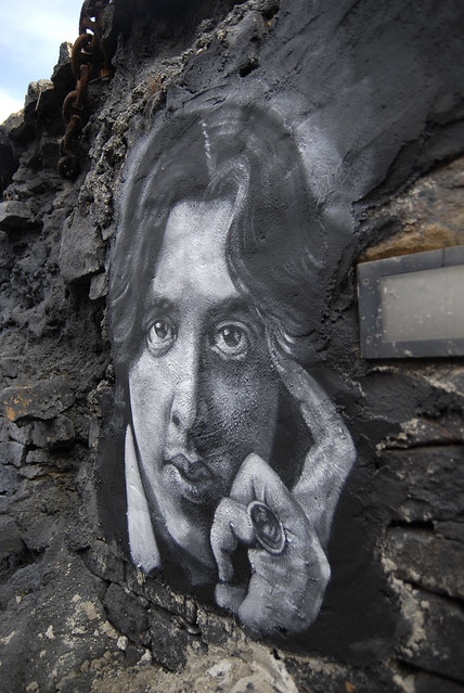 A modern graffiti portrait of Oscar Wilde on a crumbling urban wall perfectly encapsulates the Victorian period's anxiety that surface beauty could hide moral corruption.