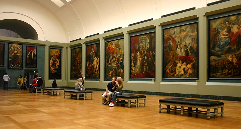 A wall in a museum with multiple pictures of paintings