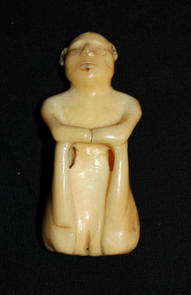A walrus tusk carved into the female body seated with her legs folded up under her arms