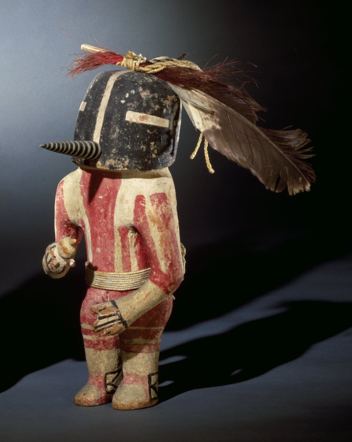 Kachina doll with feathers on its head and a painted body to represent a person