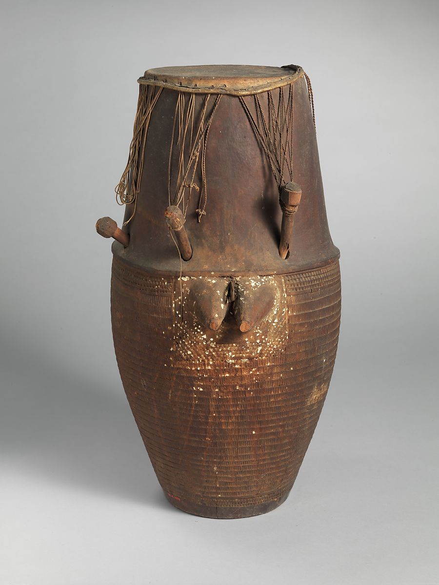 a large wooden drum with two carved breast on the side with a leather drum head