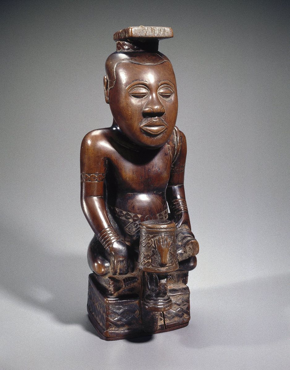 a wooden figure carved with intricate patterns and a drum in its lap