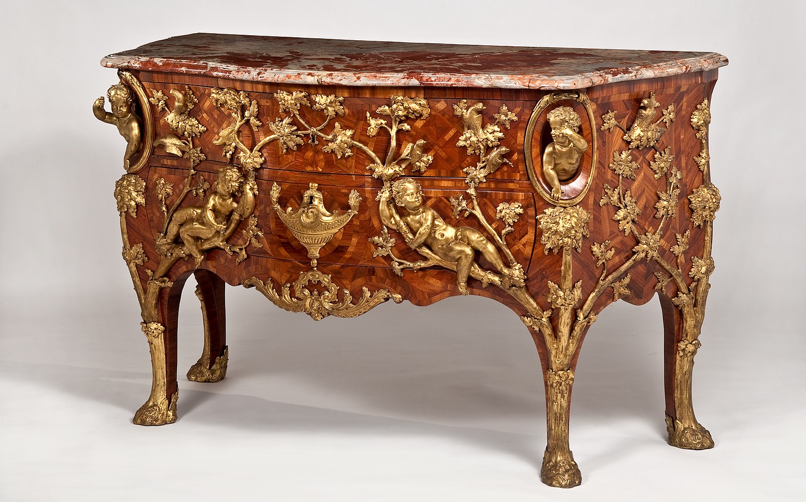 A chest of drawers with ornate gold painted figures with a dark marble top