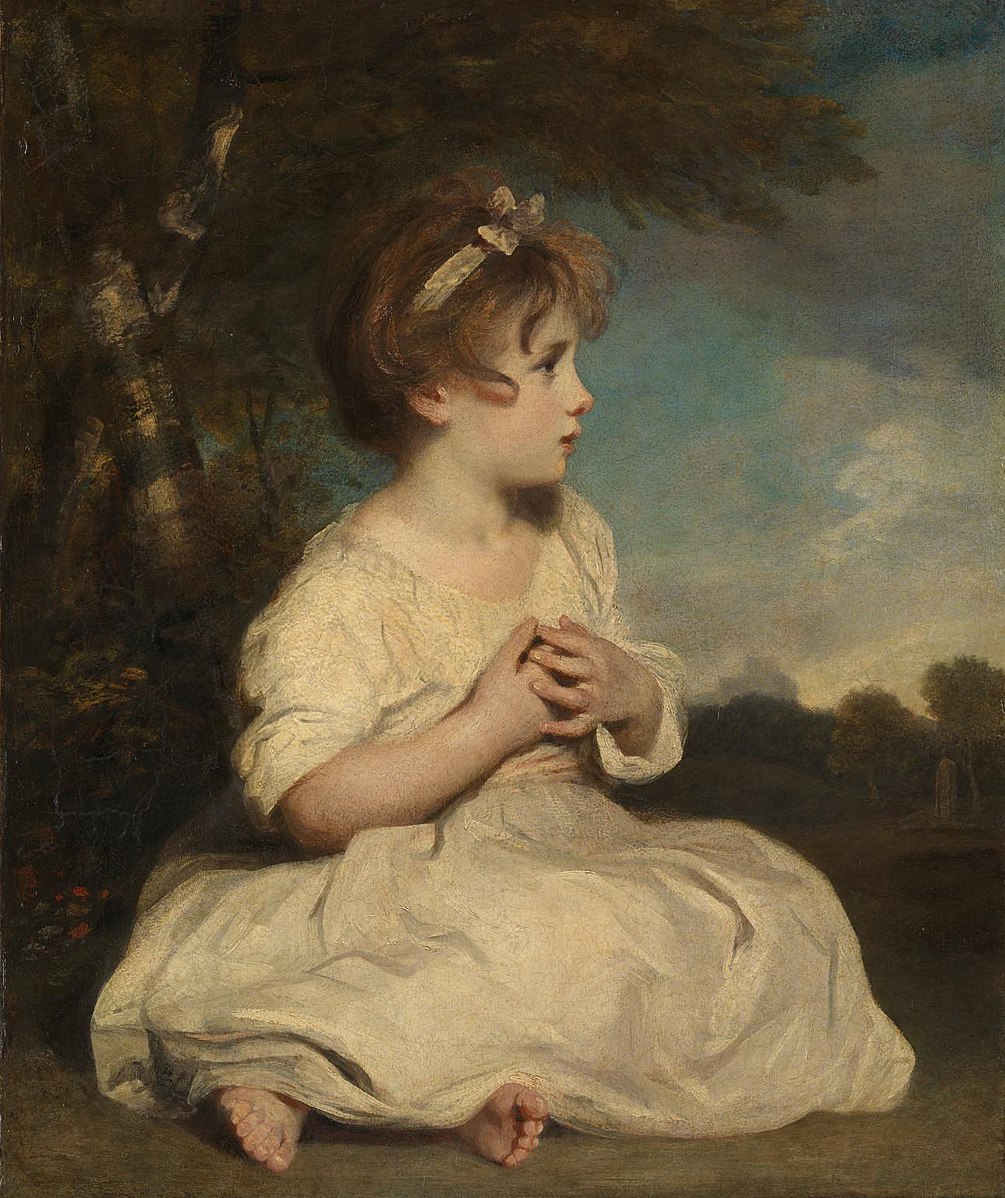 A small child in a white dress sitting on the grass with a tree 