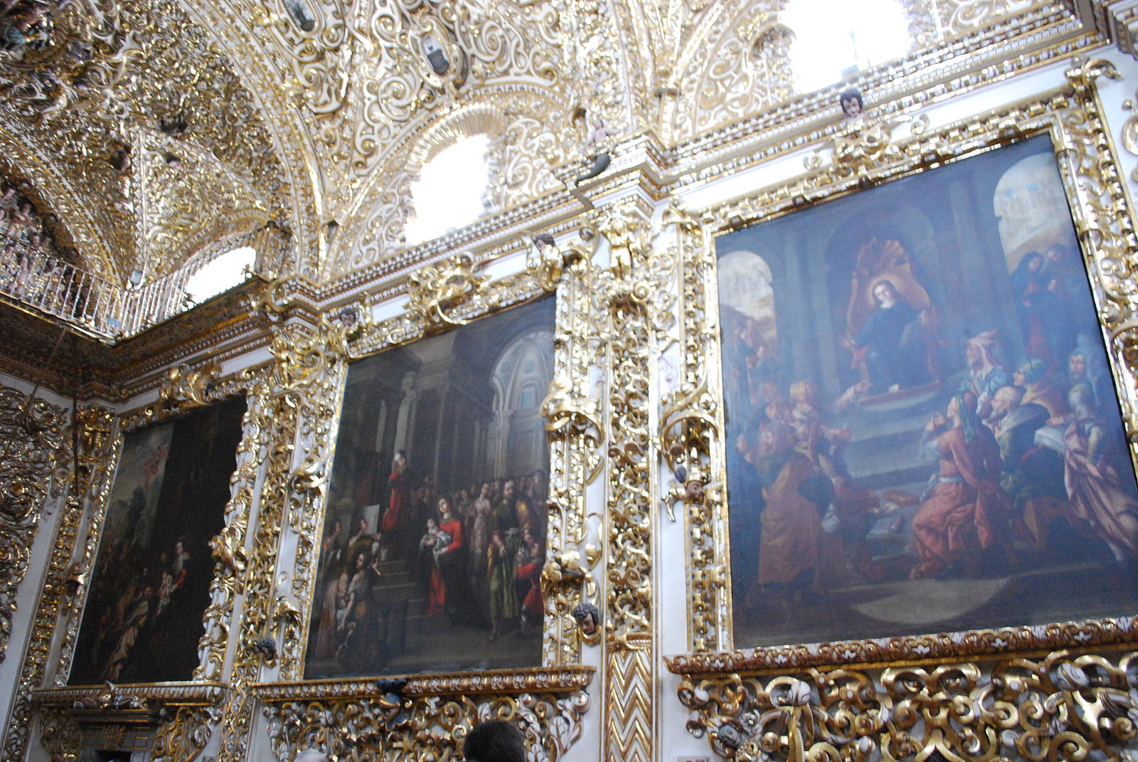 Wall in a church with ornate scroll work and paintings hanging on the wall