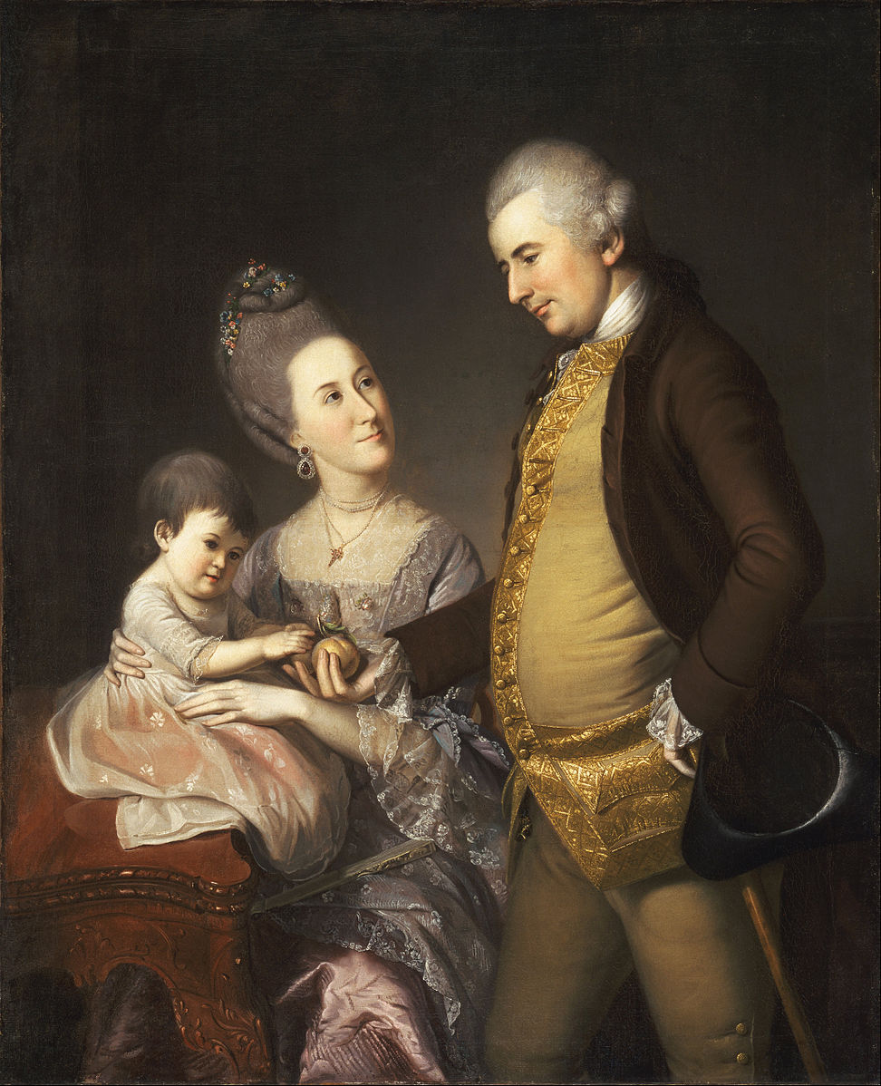A man standing, woman sitting, and child sitting with silk clothing against a dark background