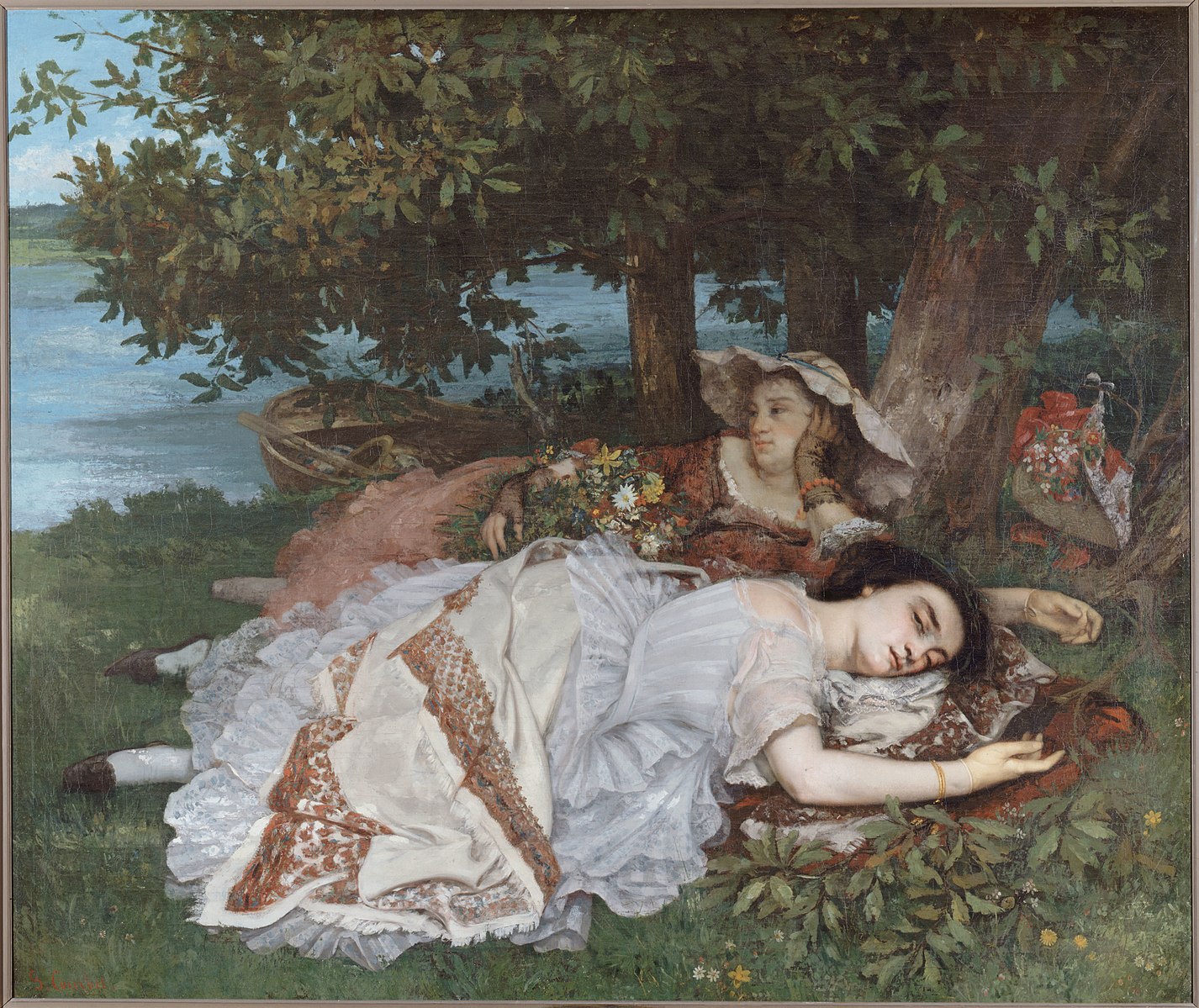 Two women laying on a blanket under a tree next to a lake