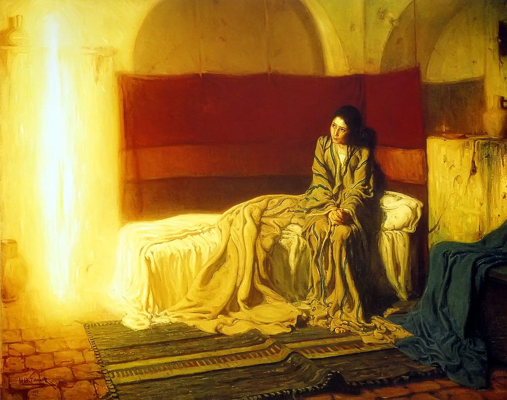 A woman sitting on a bed in a dark room looking at a glowing yellow light