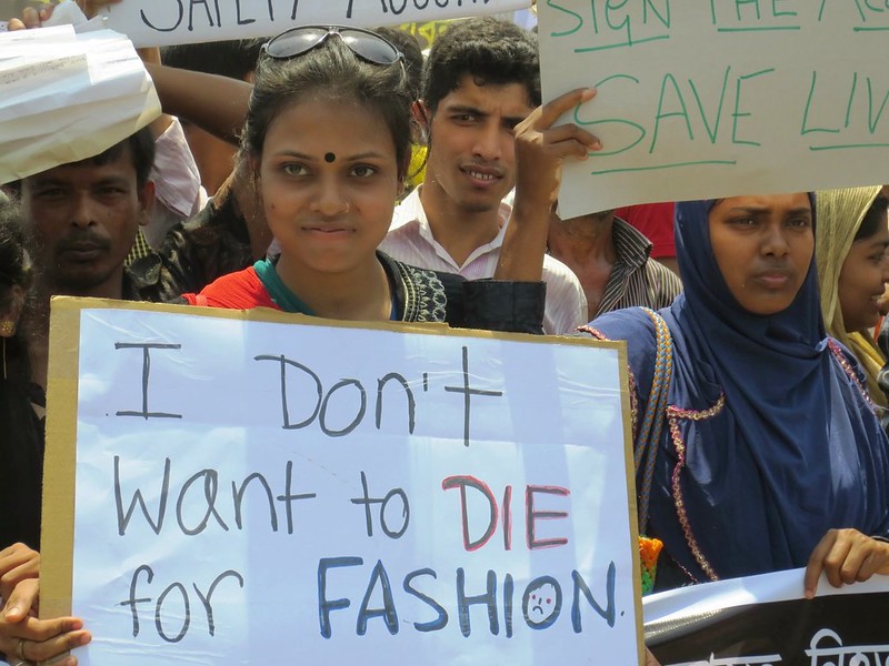 dans la foule, des jeunes femmes brandissent des pancartes faites à la main, dont l'une indique « Je ne veux pas mourir pour la mode »