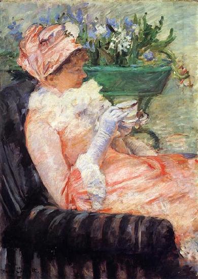 A woman dressed in pink sitting in a black chair drinking tea