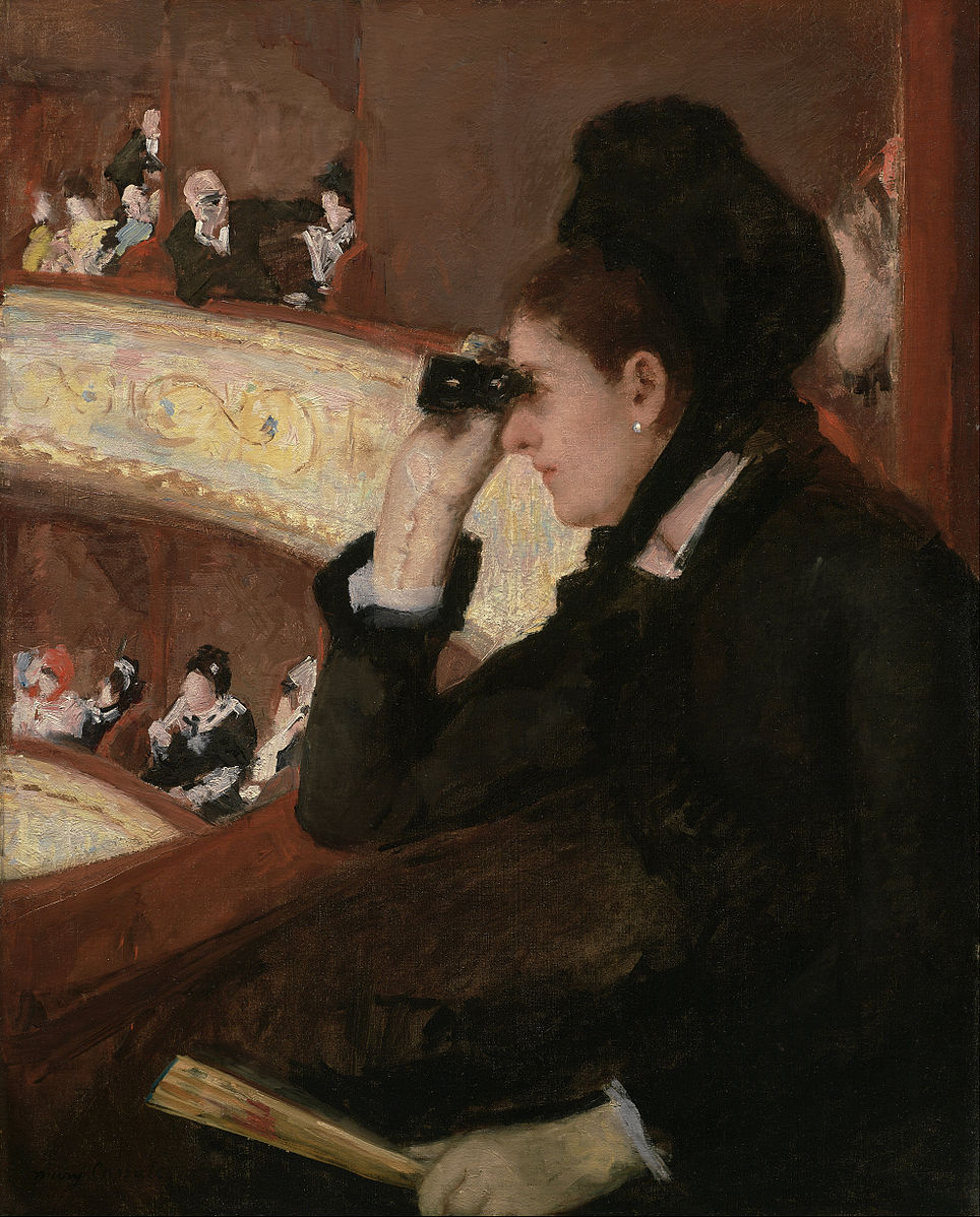 A woman dressed in black sitting in a box seat at the opera peering through glasses