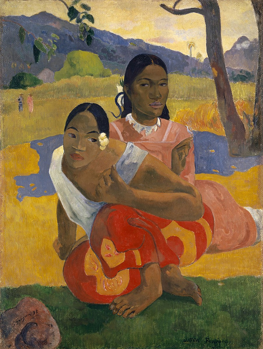 Two women sitting on grass outside with mountains in the background