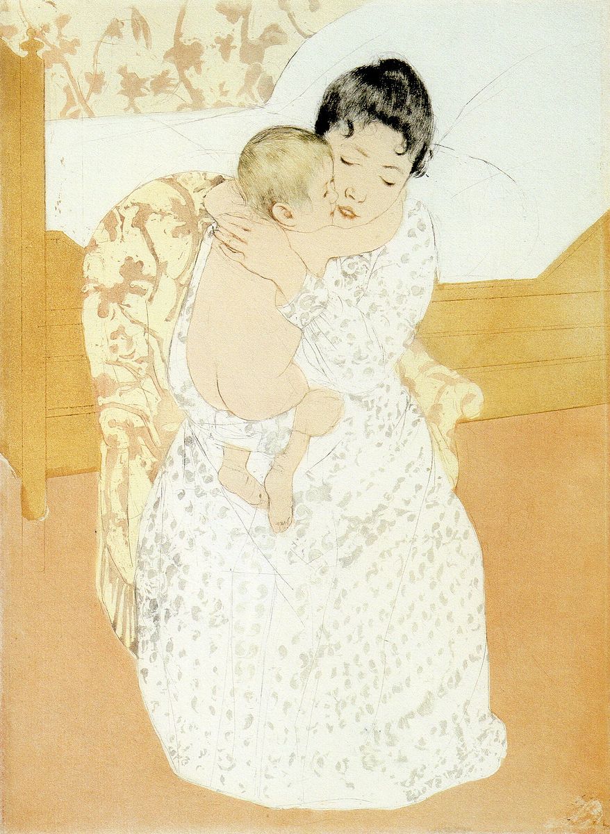 A woman in a white dress sitting in a chair next to a bed holding a baby