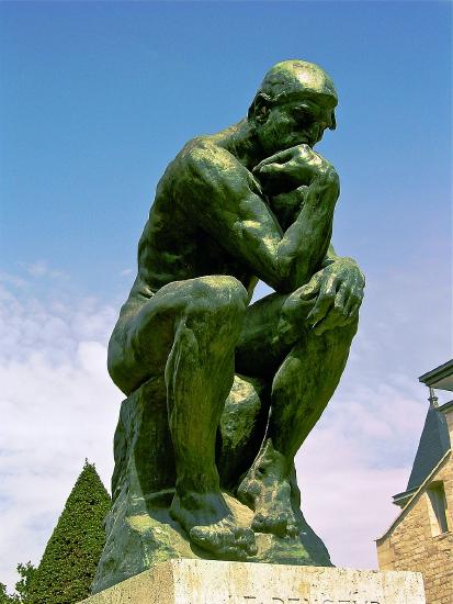 A man siting on a large rock with his chin on his hand