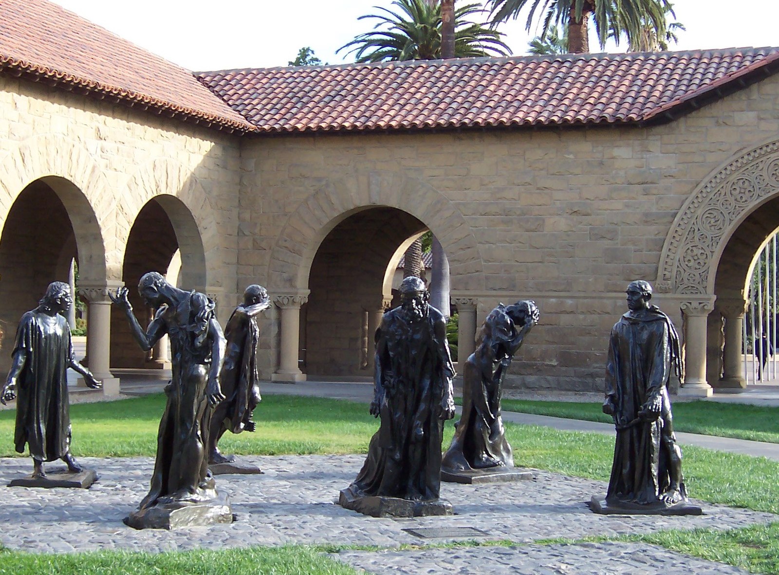 Six bronze statues of standing men on a rock base